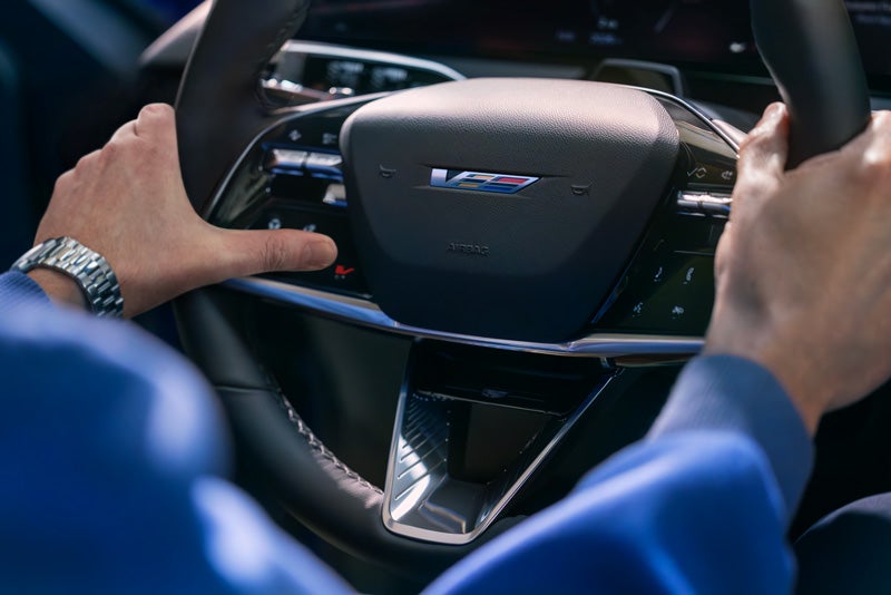 Close-up of a Man About to Press the V-Button on the 2026 OPTIQ-V Steering Wheel | Crown Cadillac in Watchung NJ